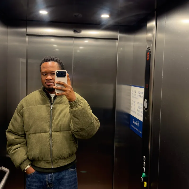 Ibukun taking a mirror selfie in a lift, wearing a green padded jacket