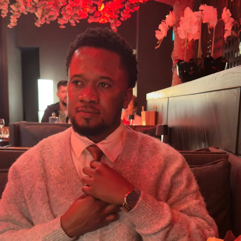Ibukun at a restaurant table under red blossom lights, adjusting a tie