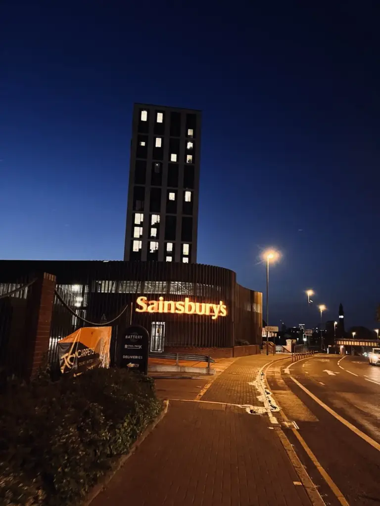 A tower block and Sainsbury's at blue hour, with street lights coming on