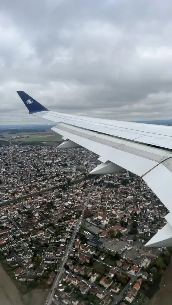 A plane wing over a city seen from above, under grey cloud