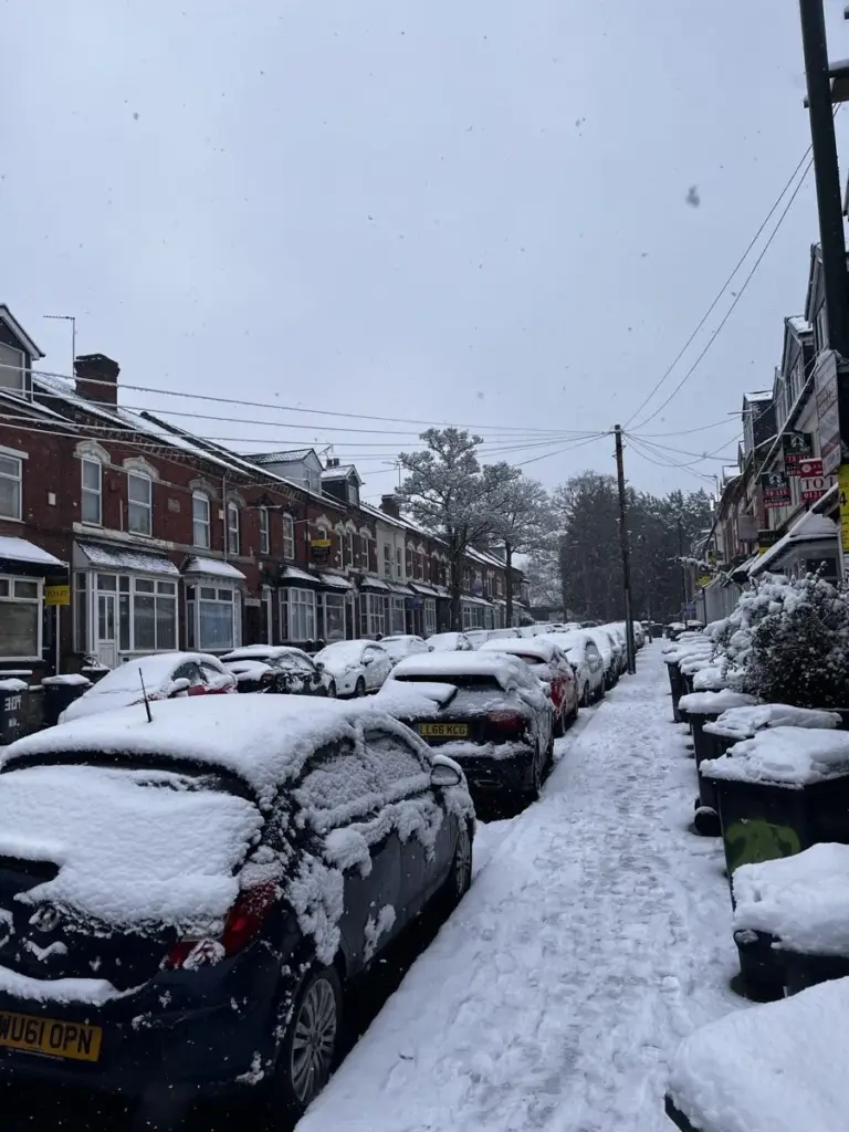A terraced street under snow, with parked cars covered white