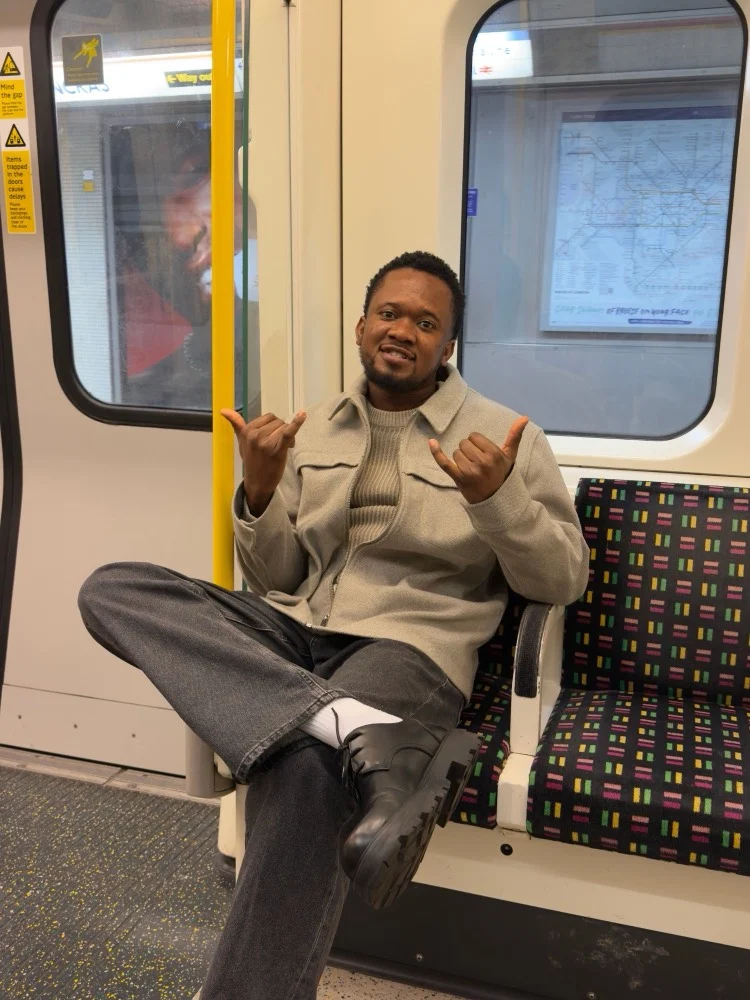 Ibukun on the London Underground, giving a shaka with both hands