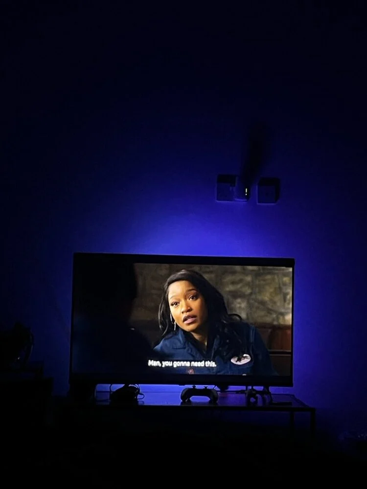 A TV glowing in a dark room lit with blue ambient light